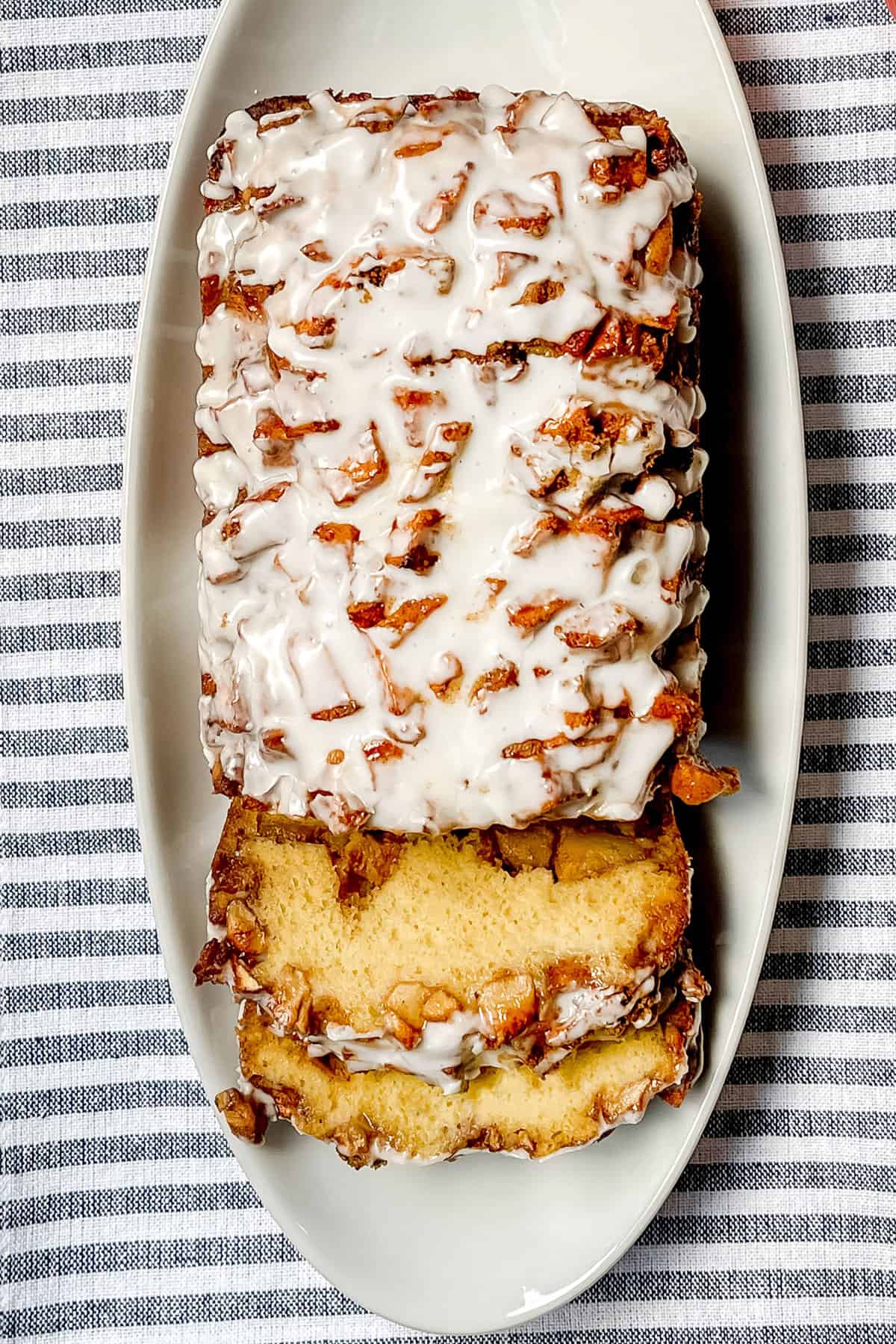 Partially sliced apple fritter bread on a white serving platter.
