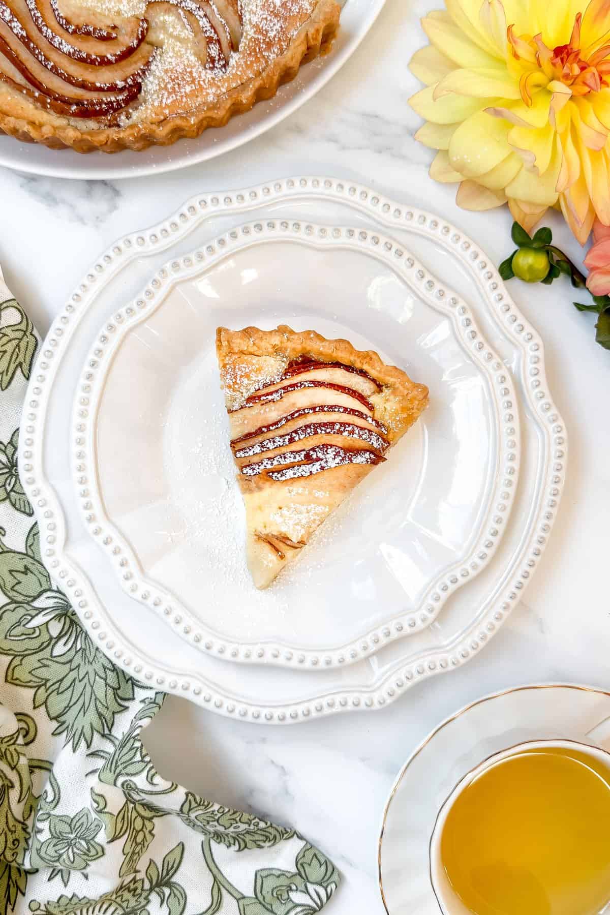 Slice of pear tart with almond filling on a white plate, ready to serve with tea.