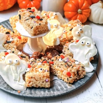 Squares of Halloween Rice Krispies Treats with white chocolate ghosts on a silver tray for serving with pumpkin in the background.