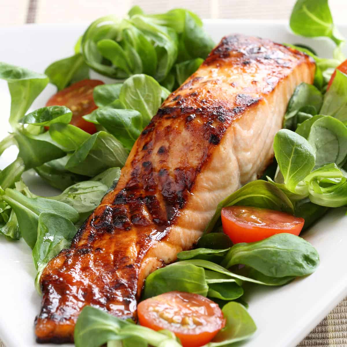 Filet of maple glazed salmon on a bed of watercress greens and sliced cherry tomatoes.