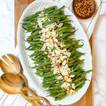 Square image of a platter filled with Green Beans Almondine arranged in rows and topped with toasted almonds and red pepper flakes.