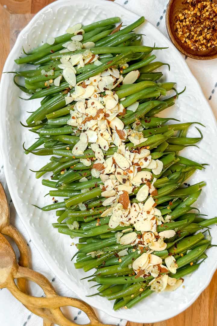 Square image of a platter filled with Green Beans Almondine arranged in rows and topped with toasted almonds and red pepper flakes.