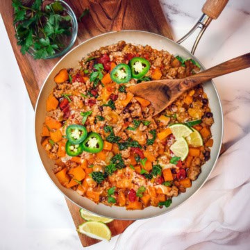 Southwestern ground turkey butternut skillet on a wooden board with a spoon and lime and jalapeño slices to garnish.