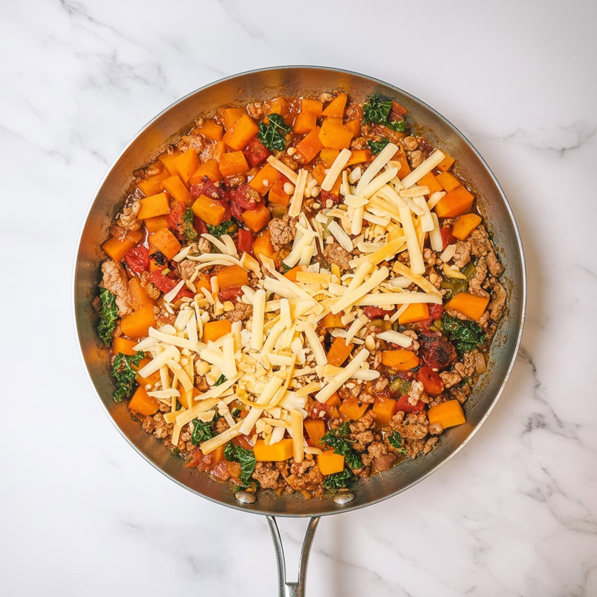 Adding cheese to the ground turkey and vegetable skillet until melted.