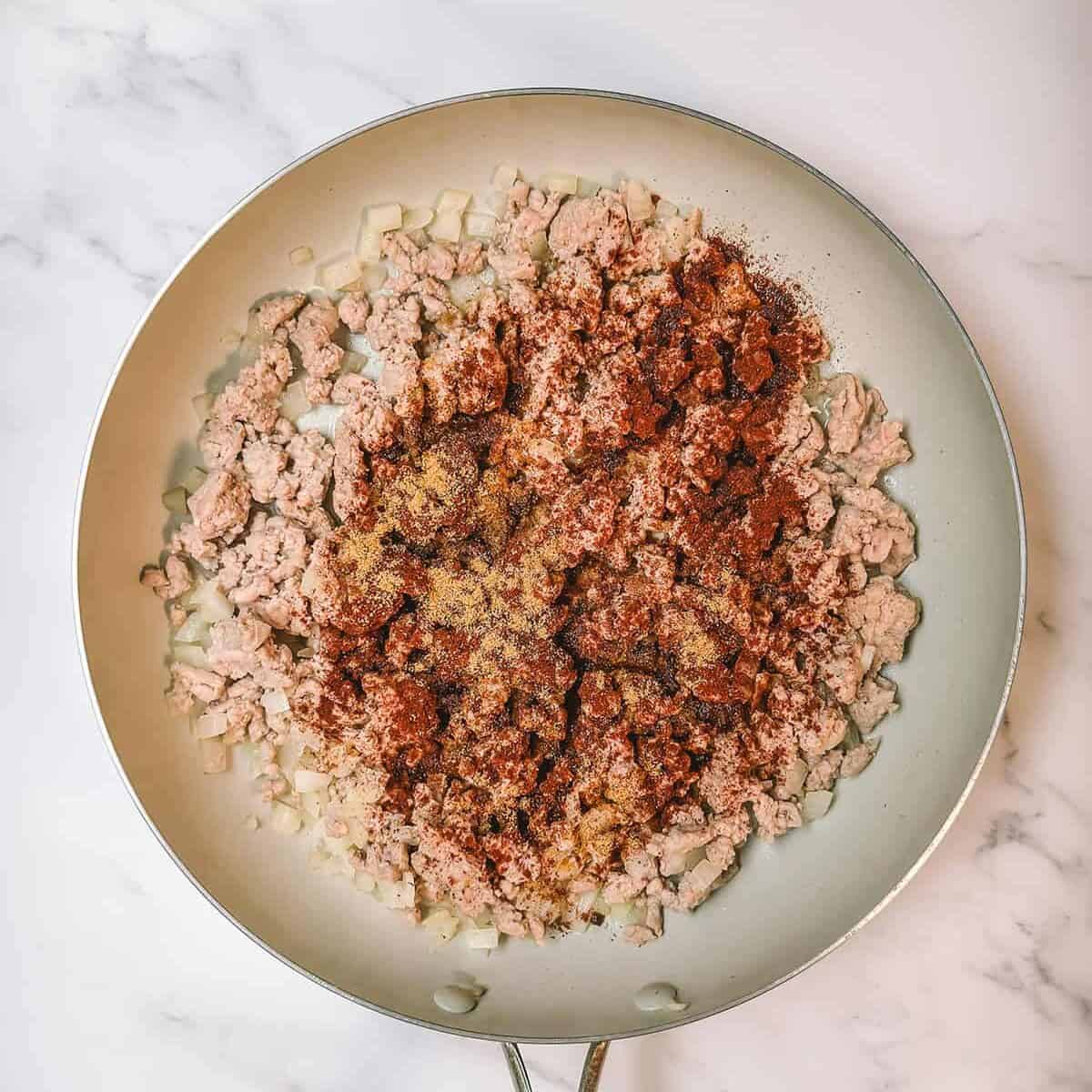 Adding spices to the browned turkey, onions, and garlic in a skillet.