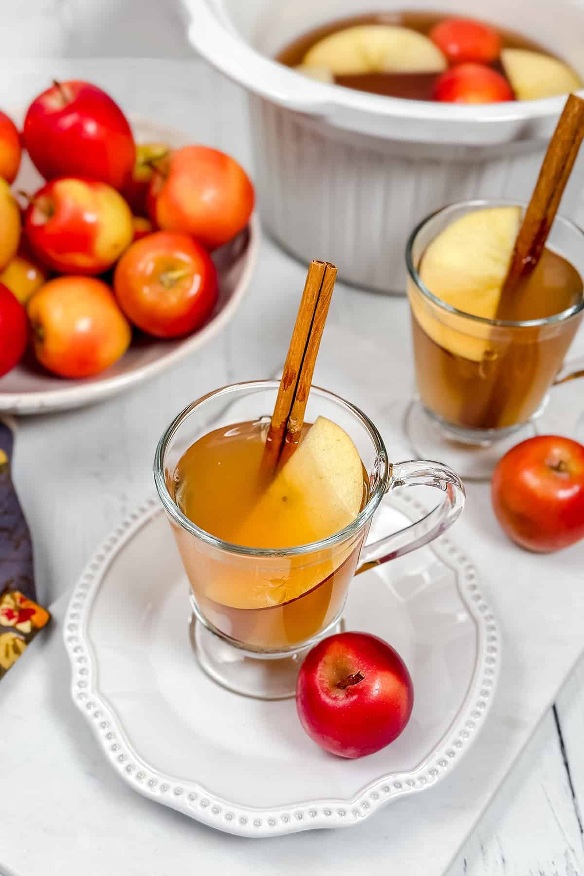 Top view of two glasses of crockpot apple cider with a bowl of apples in the background.