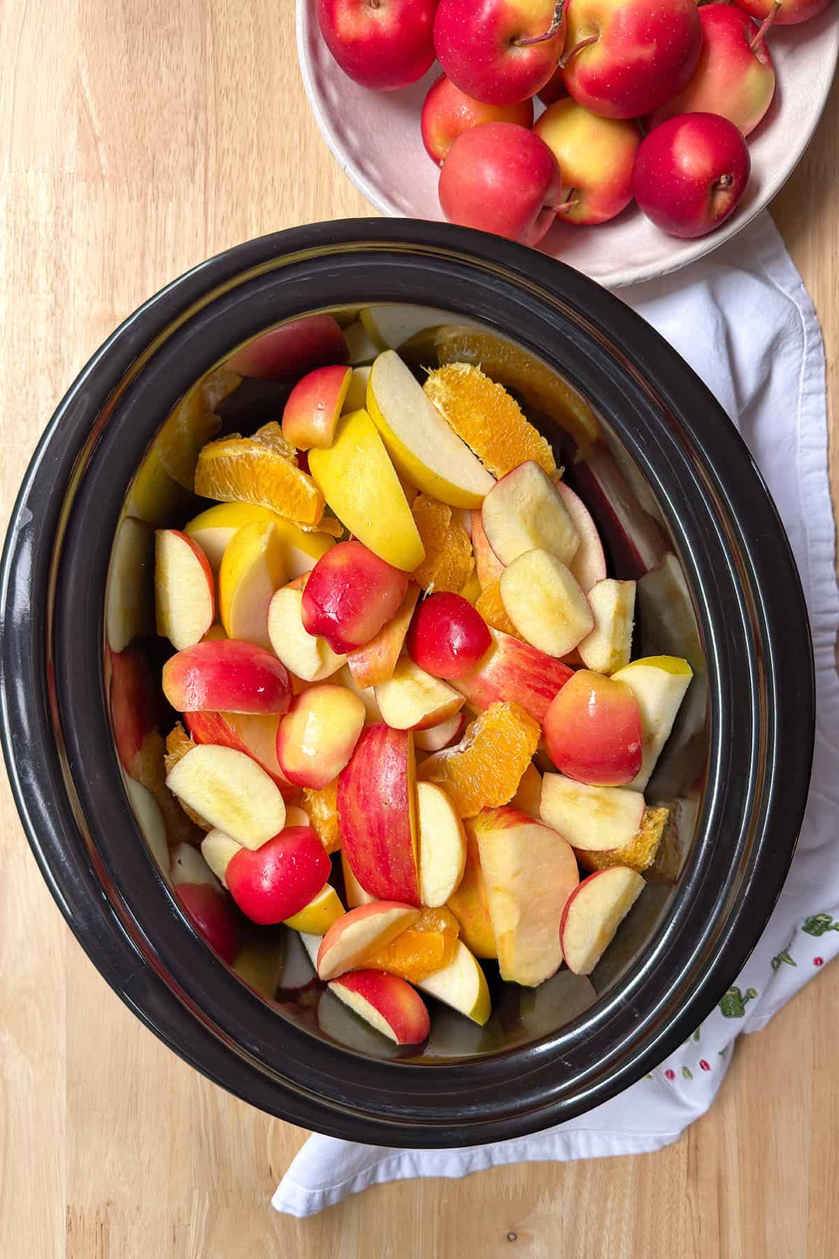 Sliced apples and oranges in a slow cooker insert.
