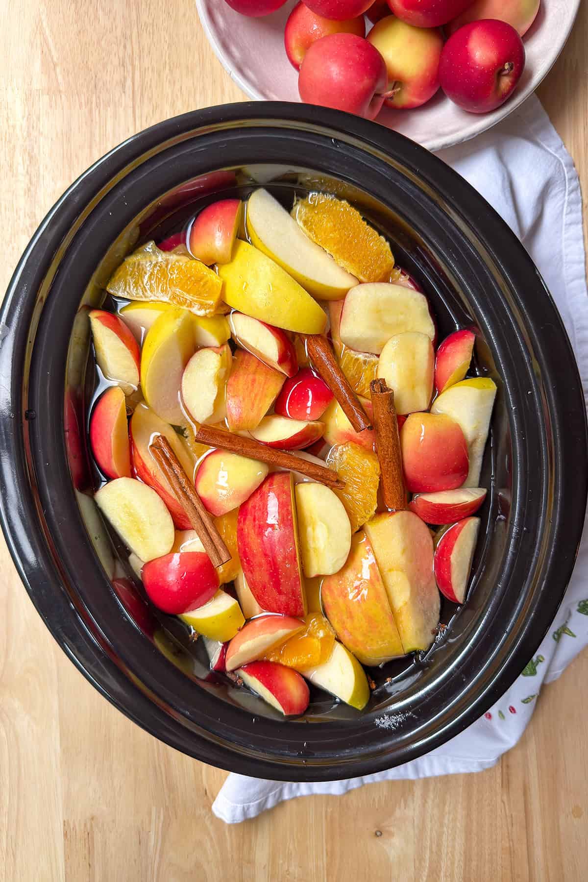 Water covering apple and orange slices with cinnamon sticks.