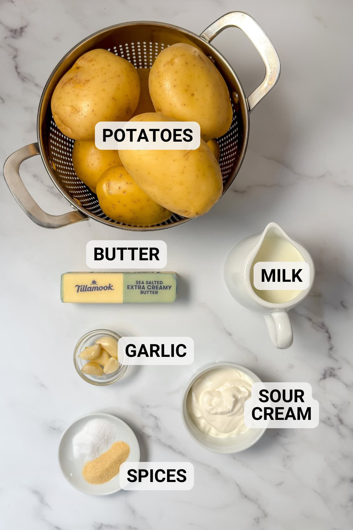 Ingredients for creamy garlic mashed potatoes including potatoes, butter, milk, garlic, sour cream, and seasonings.