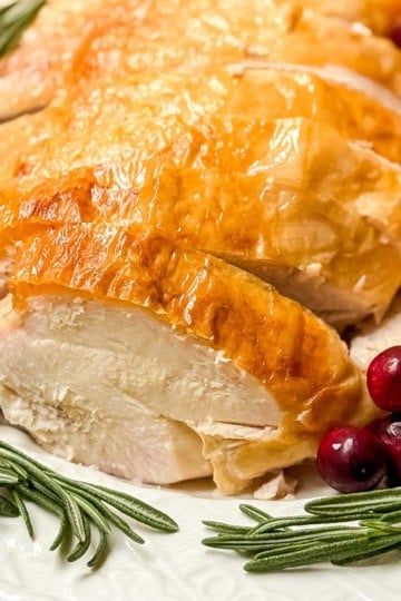 Sliced turkey breast with crispy skin on a platter with fresh rosemary and cranberries.