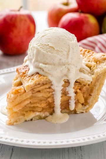Square image of sliced apple pie with fresh apples in the background and a sliced apple pie.