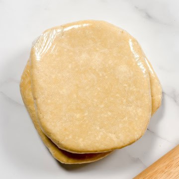 Square image of chilled and wrapped all butter crust with a rolling pin.