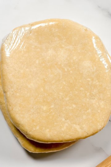 Square image of chilled and wrapped all butter crust with a rolling pin.