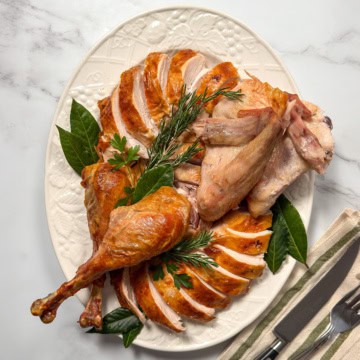 Carved roast turkey arranged on a large white platter with fresh herbs ready for serving.