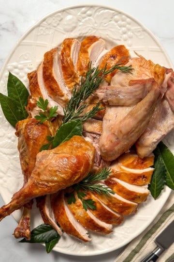 Carved roast turkey arranged on a large white platter with fresh herbs ready for serving.