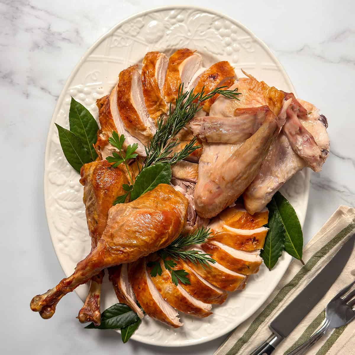 Carved roast turkey arranged on a large white platter with fresh herbs ready for serving.