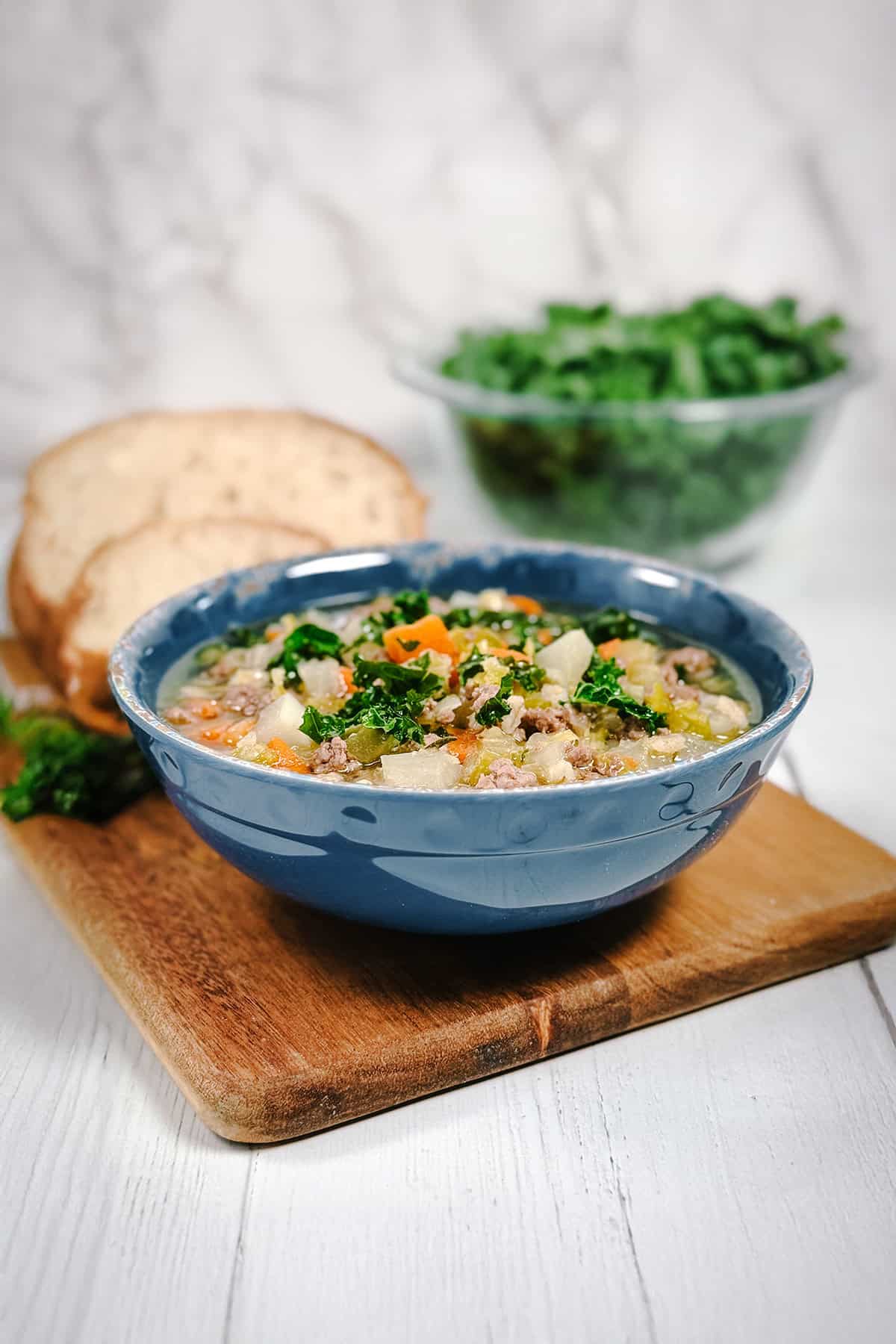 Scotch Broth lamb and barley soup in a bowl, topped with kale with sourdough bread slices in the background.