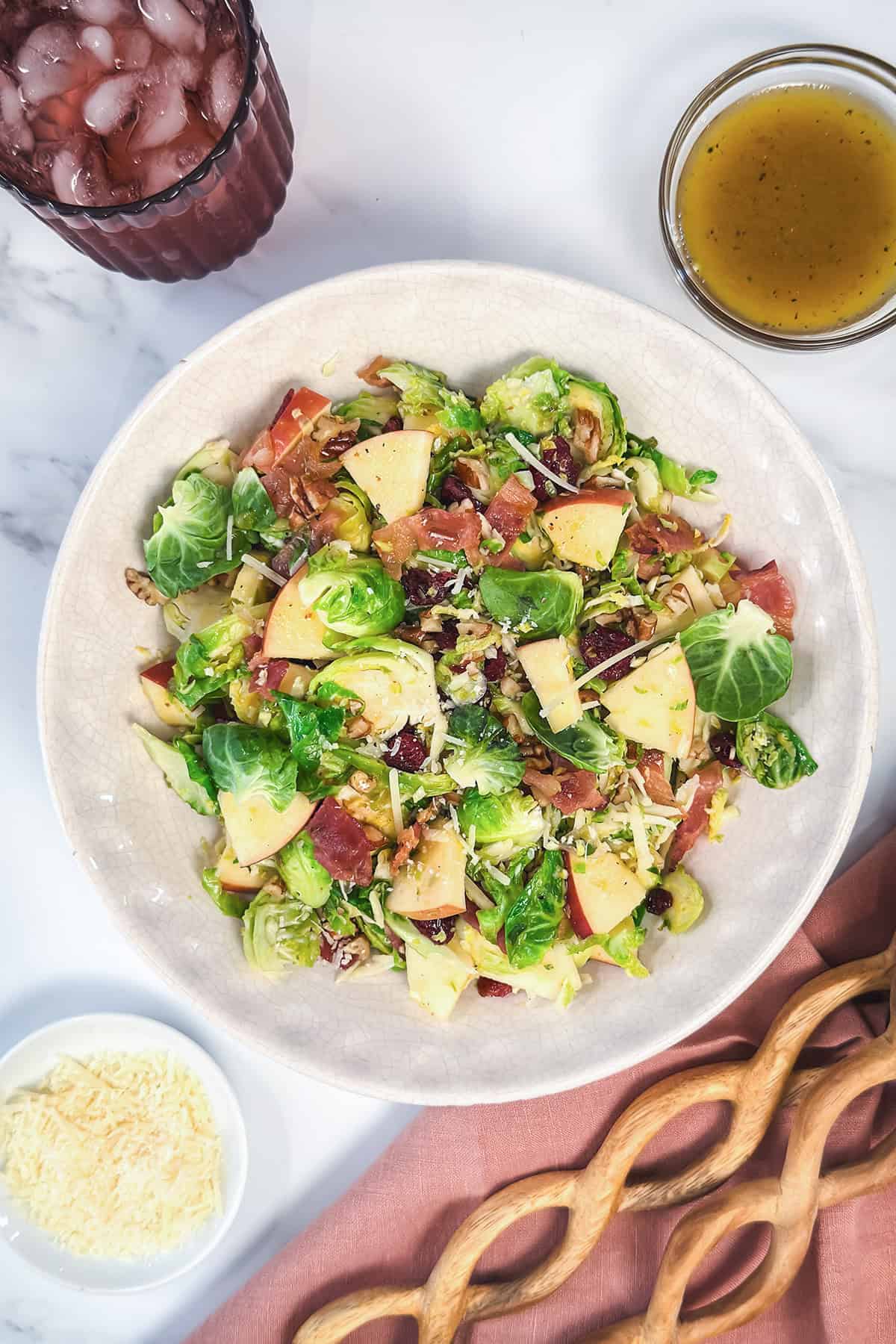 Warm Brussels Sprouts Salad in a large bowl topped with chopped apples, toasted pecans, and crispy bacon.