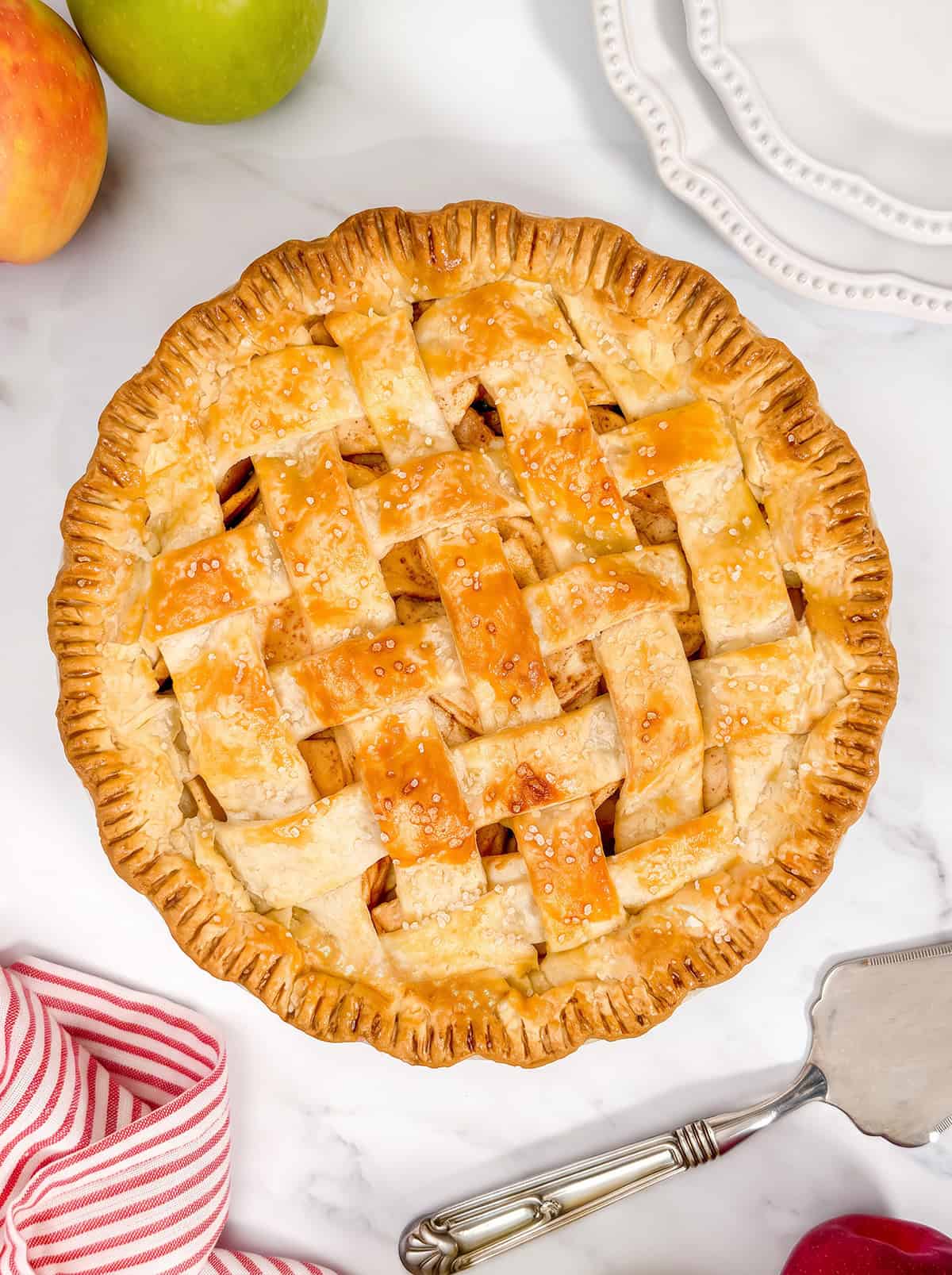 Top view of lattice apple pie on a marble surface with fresh apples nearby.