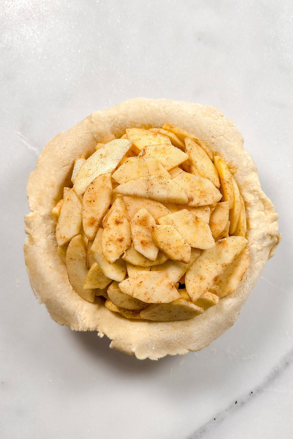 Spiced sliced apples in a crust lined pie plate ready for the top crust.