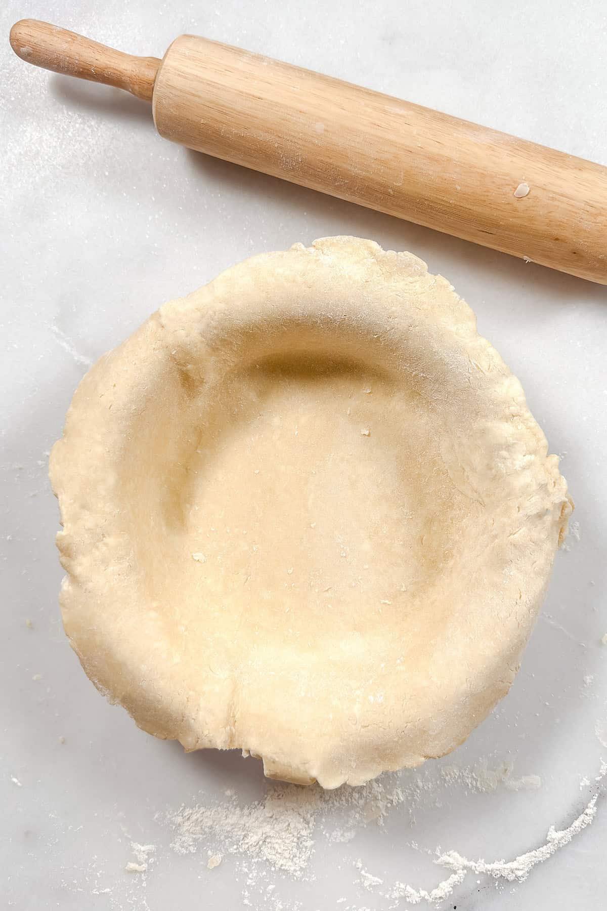 An unbaked pie crust lining a pie plate with dough overhang on all sides.