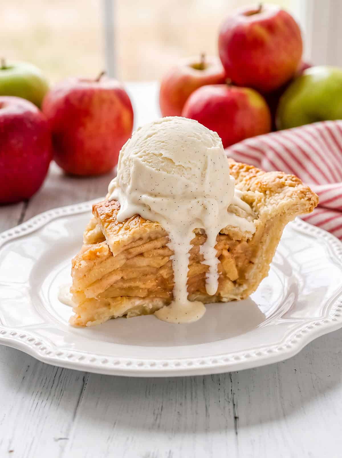 Slice of apple pie with a lattice all butter crust and a scoop of vanilla ice cream on top.