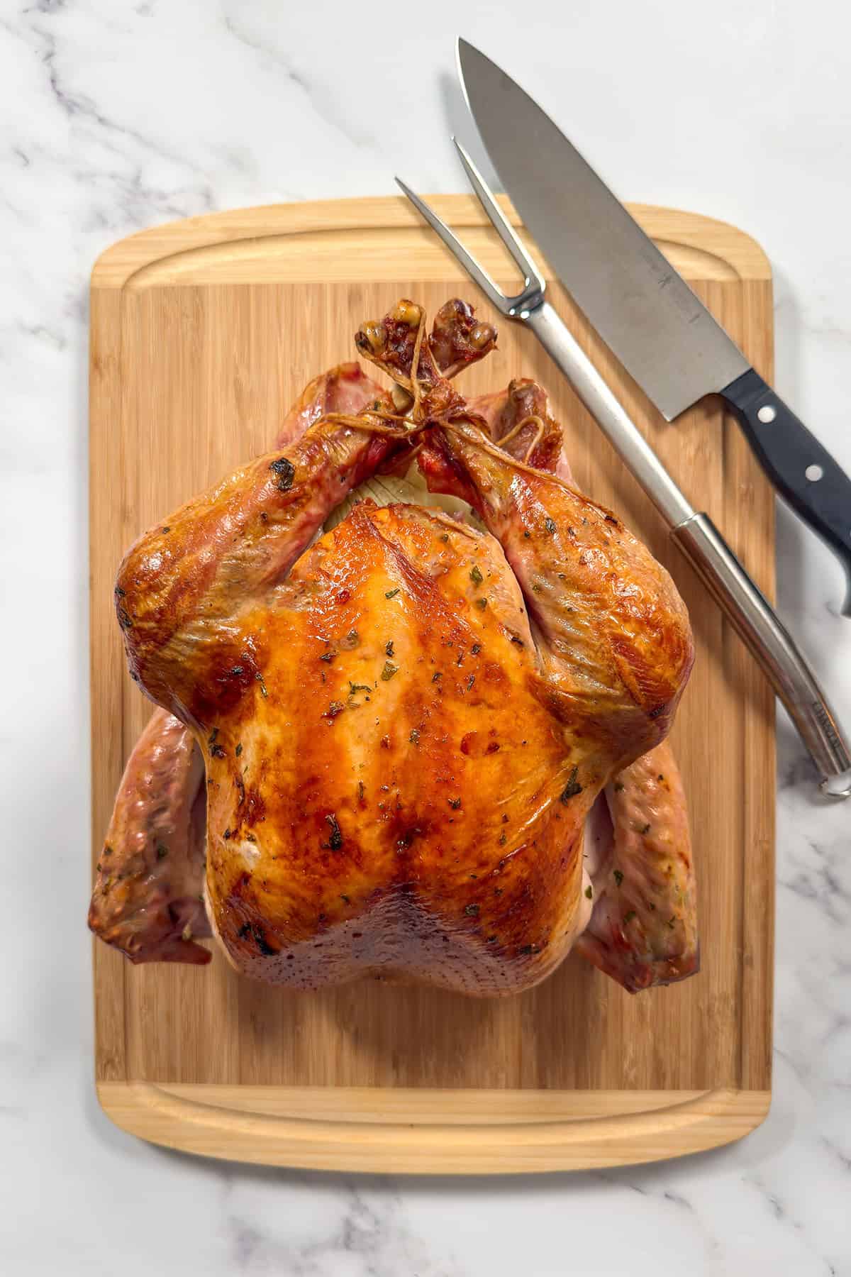 Whole roasted turkey on a wooden cutting board with carving knife and fork, ready to carve.