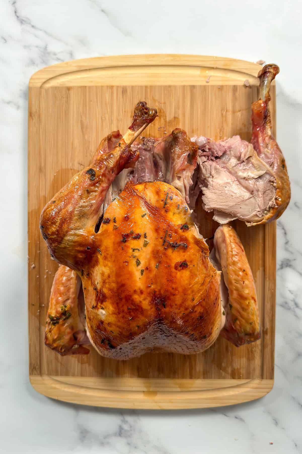 Whole roasted turkey on a bamboo cutting board with right leg thigh quarter removed.