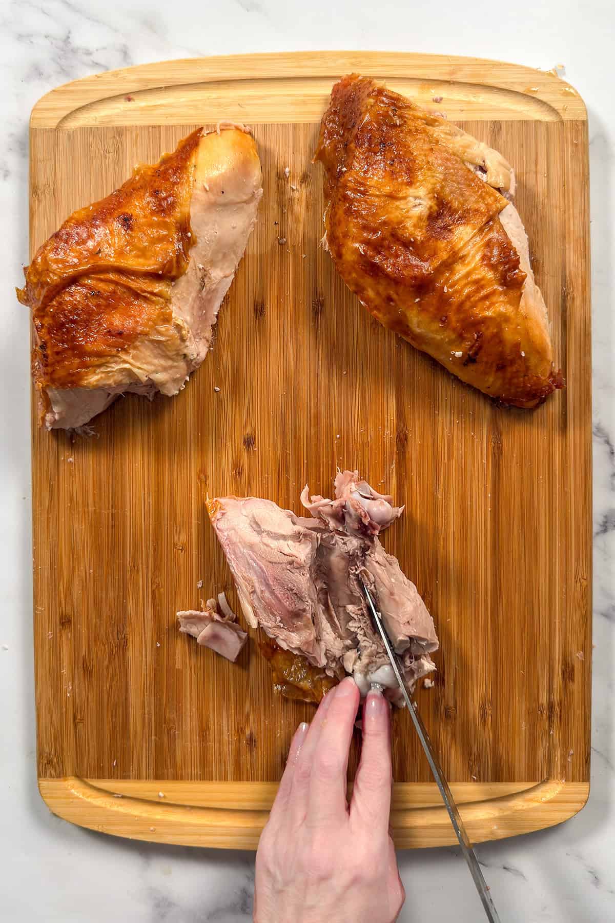 Removing bone from turkey thigh on wooden cutting board.