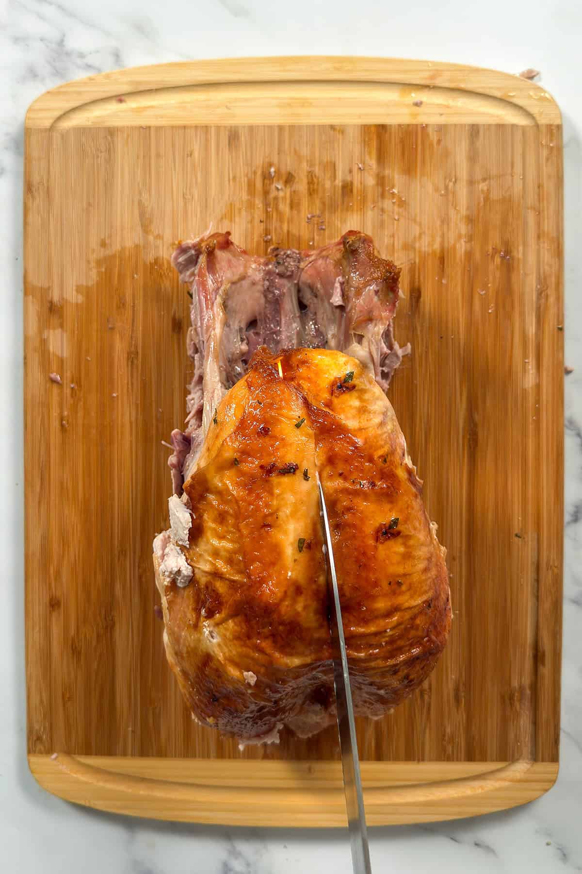 Whole roasted turkey on a bamboo cutting board with shape chef's knife scoring the breast skin. 
