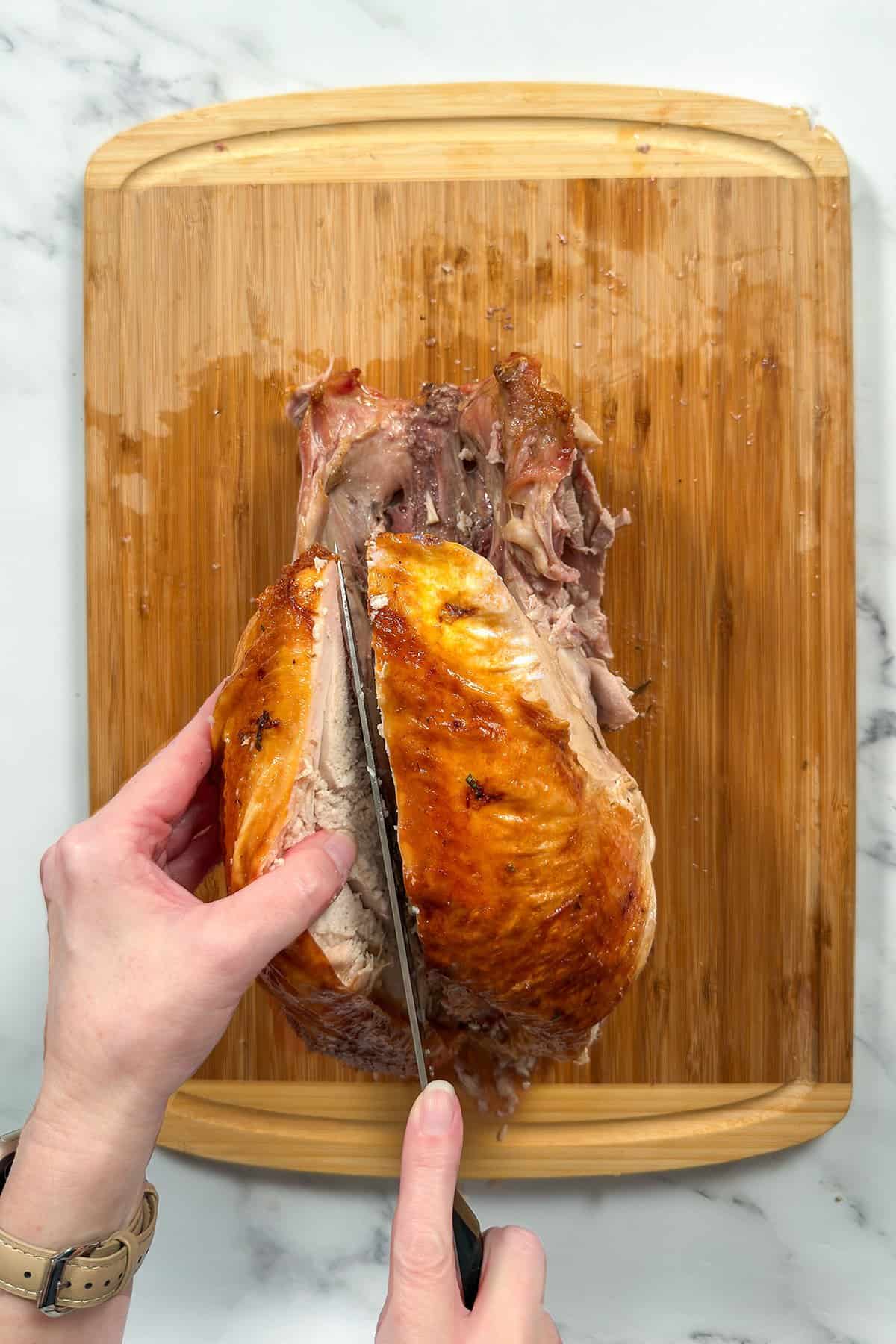 Whole roasted turkey on a bamboo cutting board with a sharp knife separating the breast meat from the carcass. 