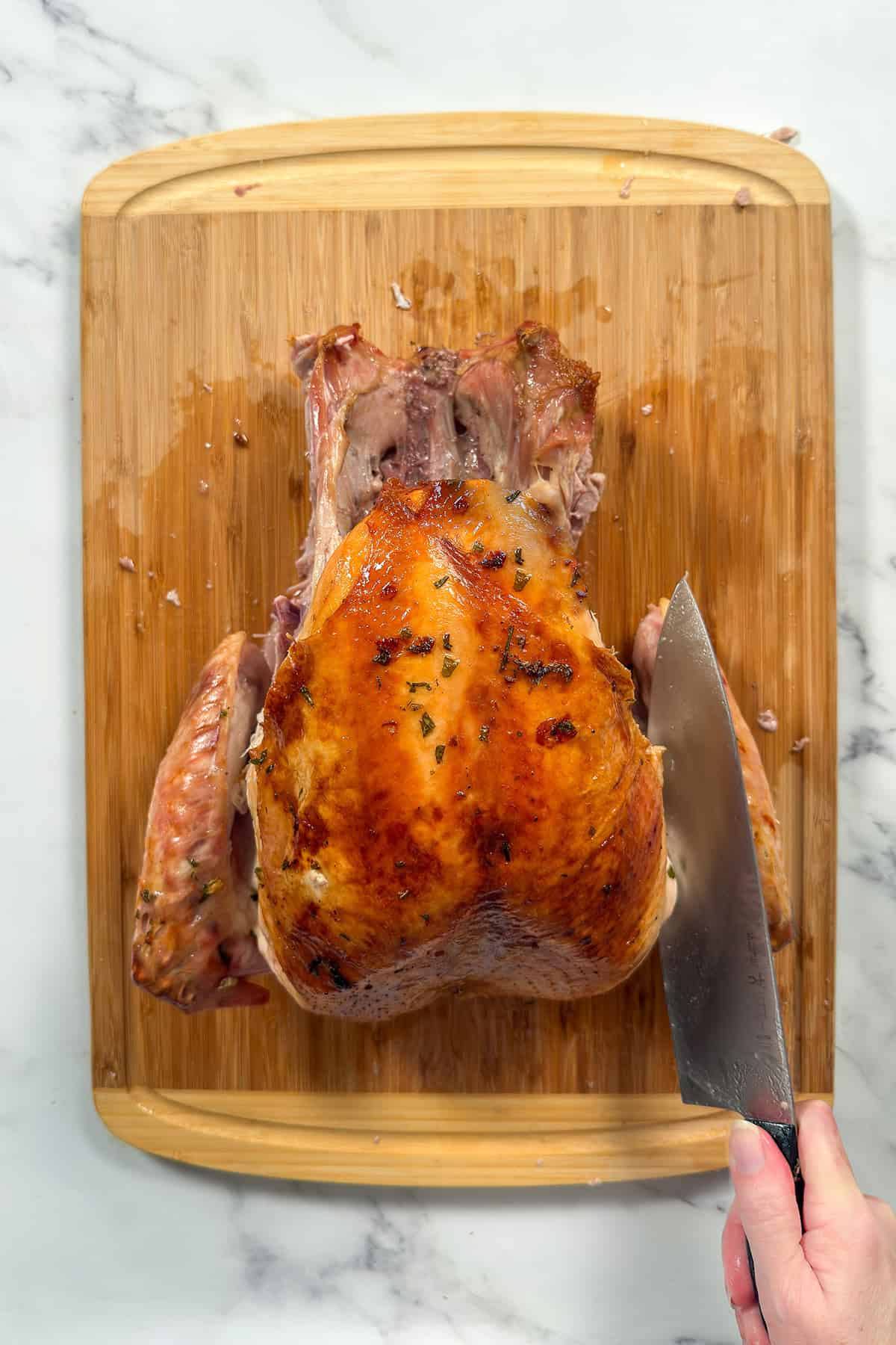 Whole roasted turkey on a bamboo cutting board with right wing being separated with a large knife.