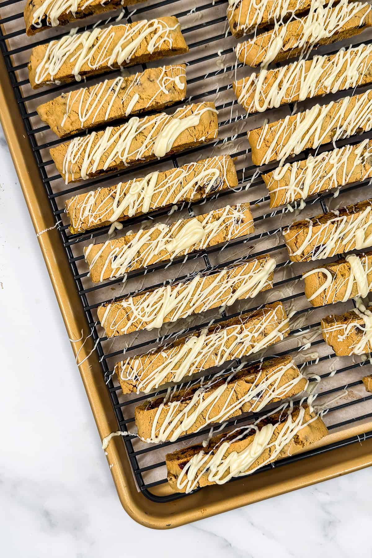 Drizzling glaze over twice baked biscotti slices on a rack.