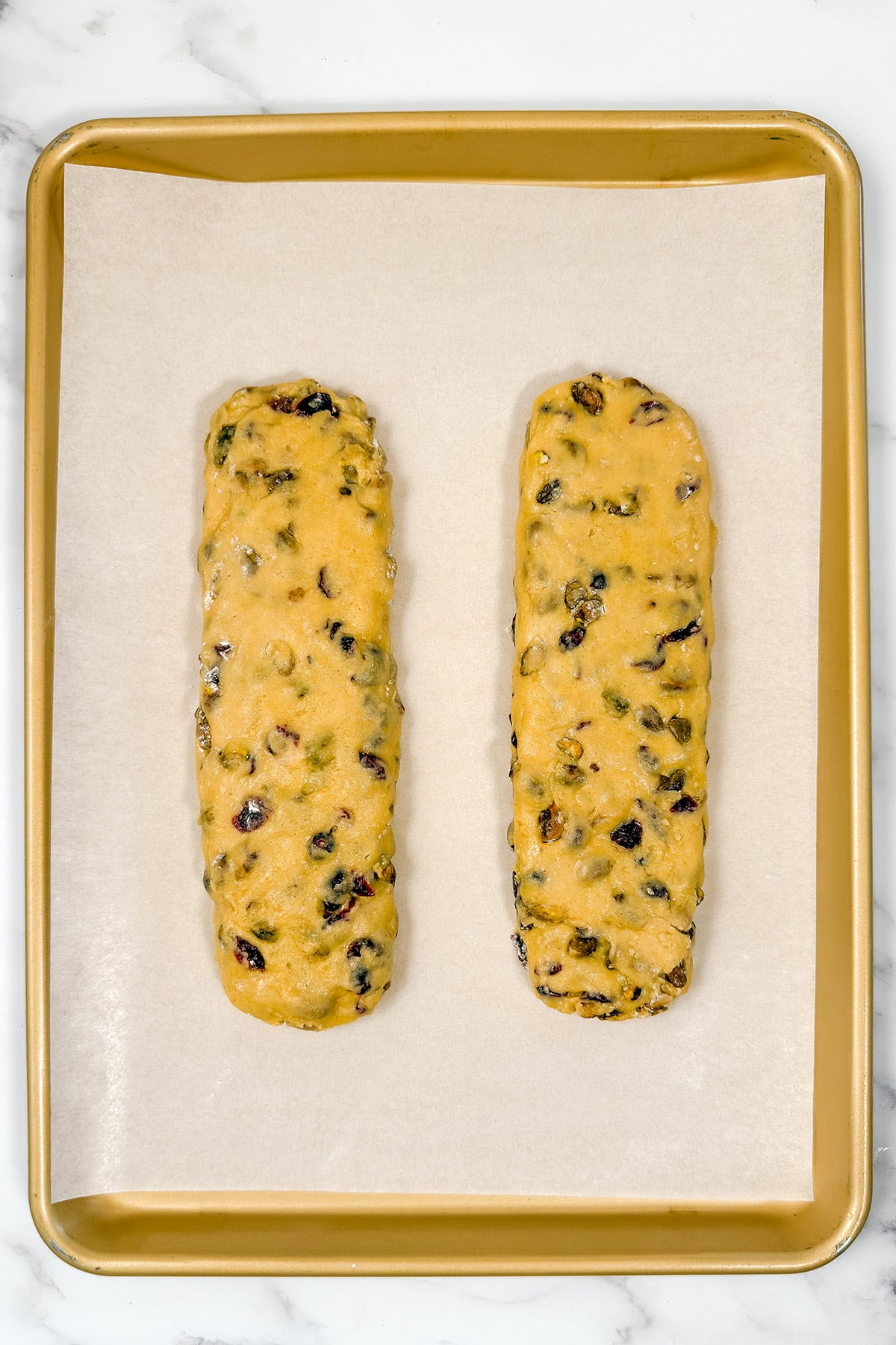 Two logs of unbaked cranberry pistachio biscotti dough on parchment lined baking sheet.