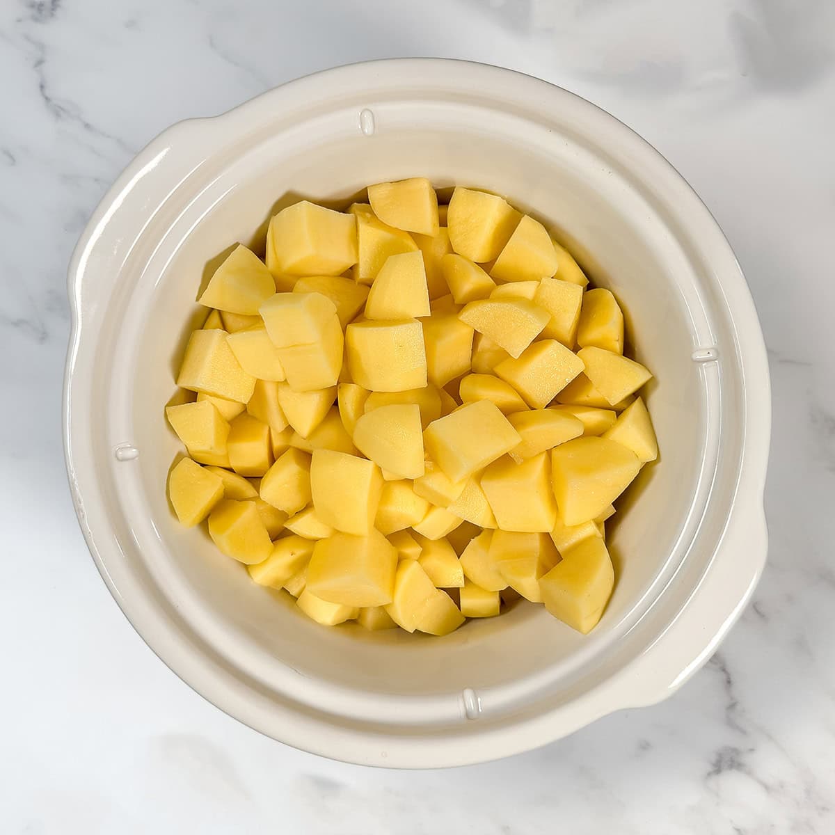 Chopped potatoes, water, and seasoning in a crockpot insert waiting for cooking.