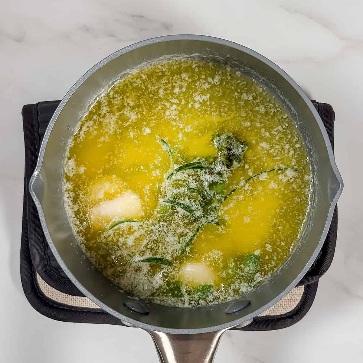 Infusing butter with garlic and fresh herbs in a small saucepan for crockpot mashed potatoes.