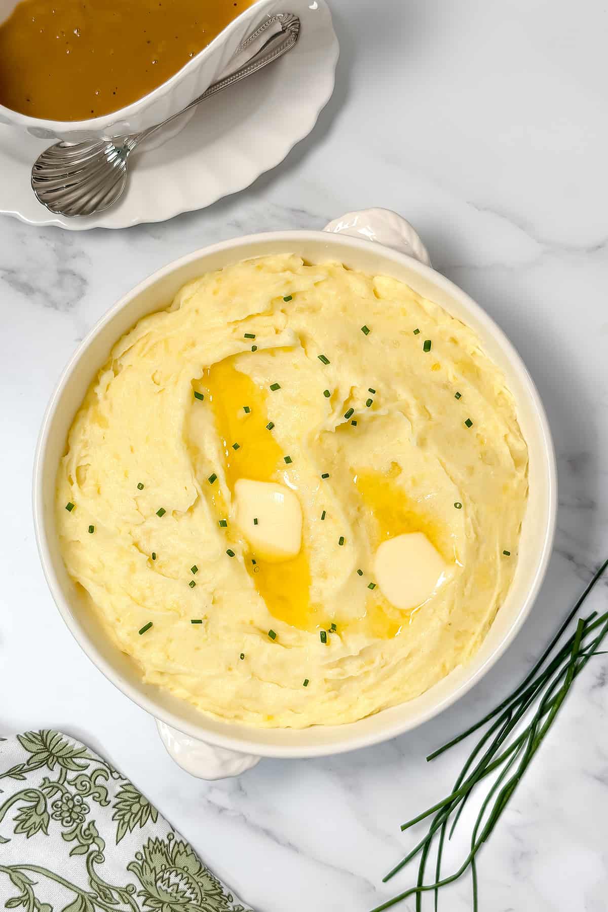 Top view of garlic mashed potatoes topped with fresh chives and pats of butter melting into the potatoes.