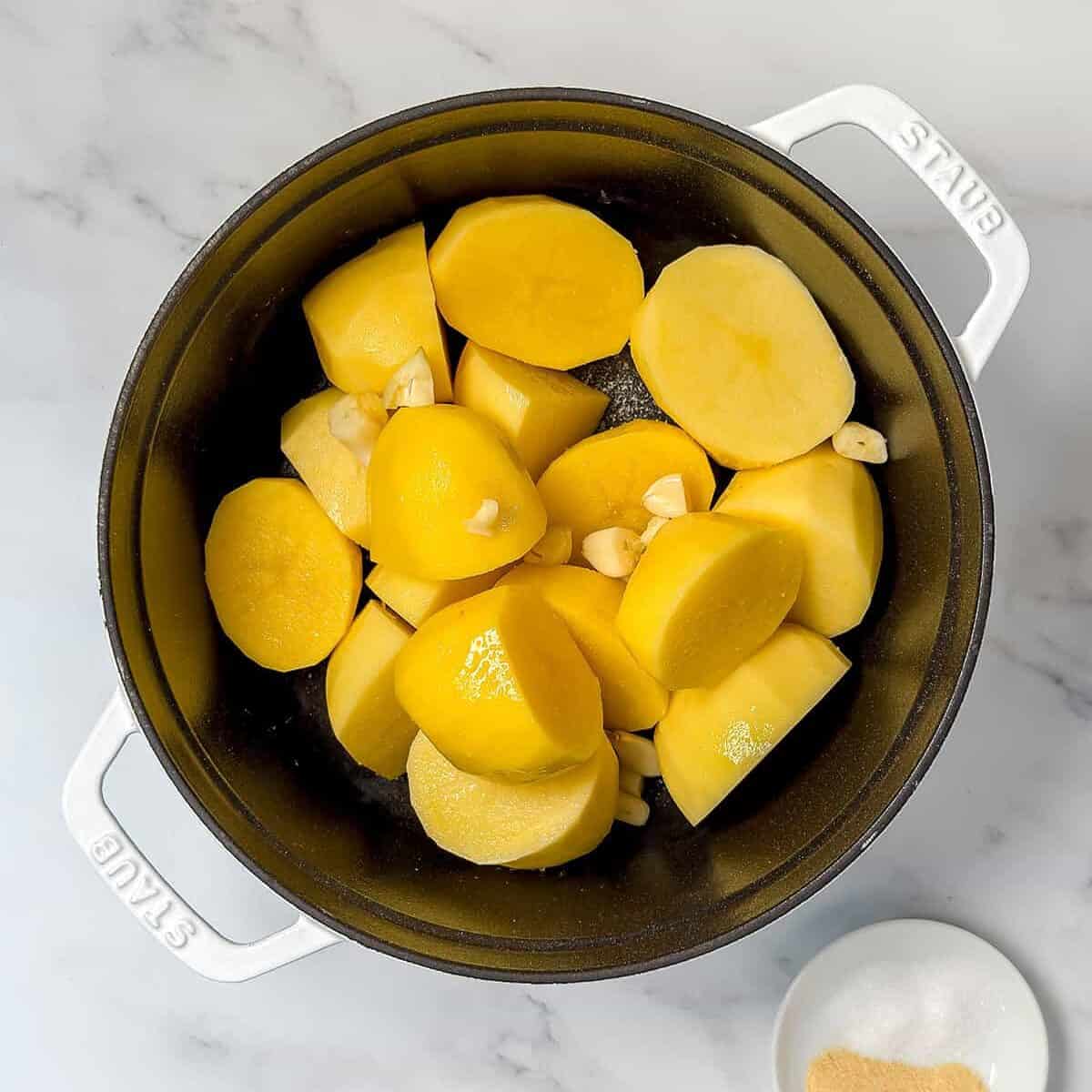 Cut potatoes and garlic cloves in a large Dutch oven with salt and garlic powder on the side.