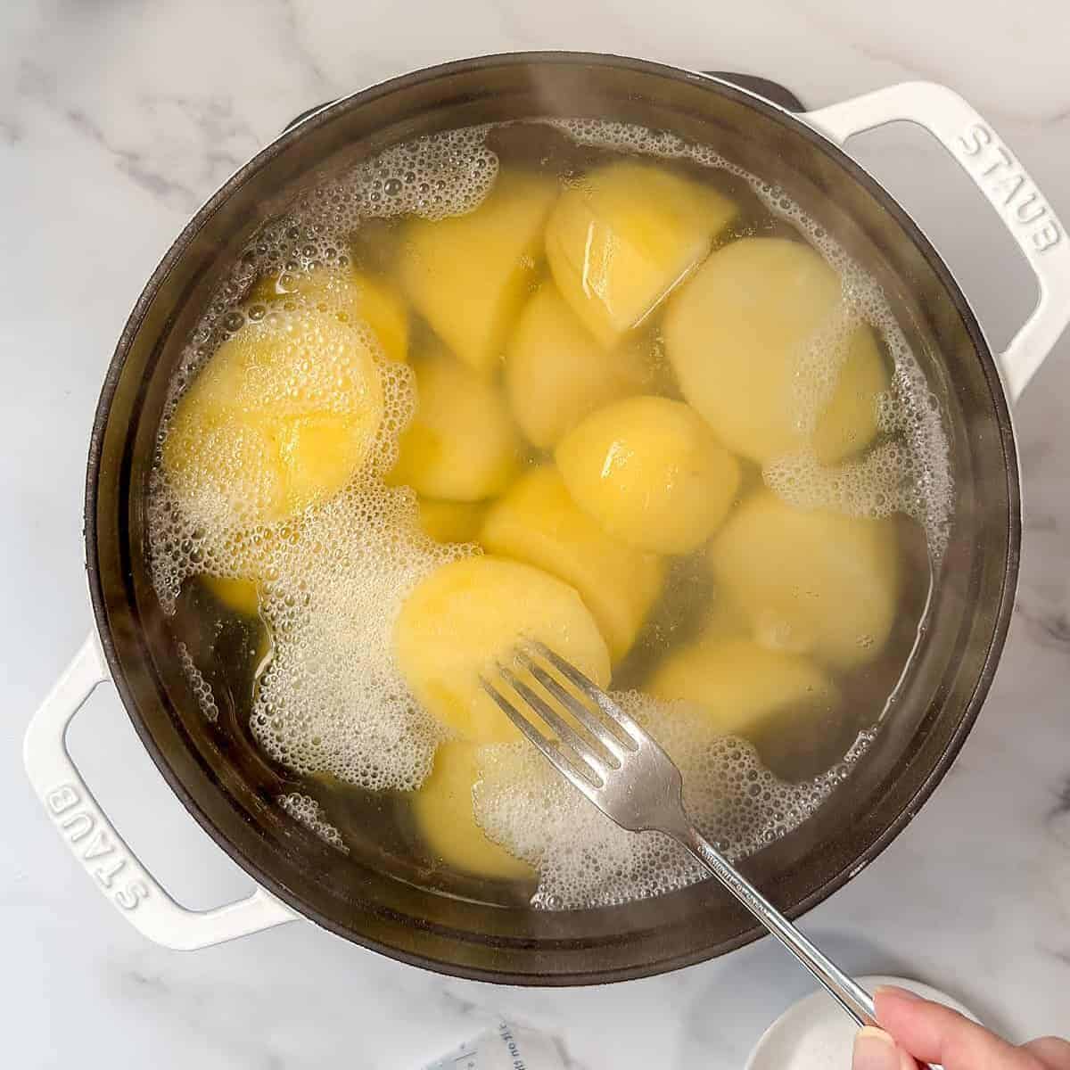 Cooked potatoes in a large pot with a fork testing softness.