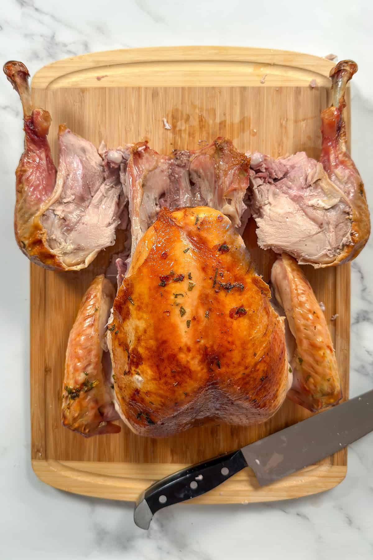 Whole roasted turkey on a bamboo cutting board with both leg thigh quarters removed.