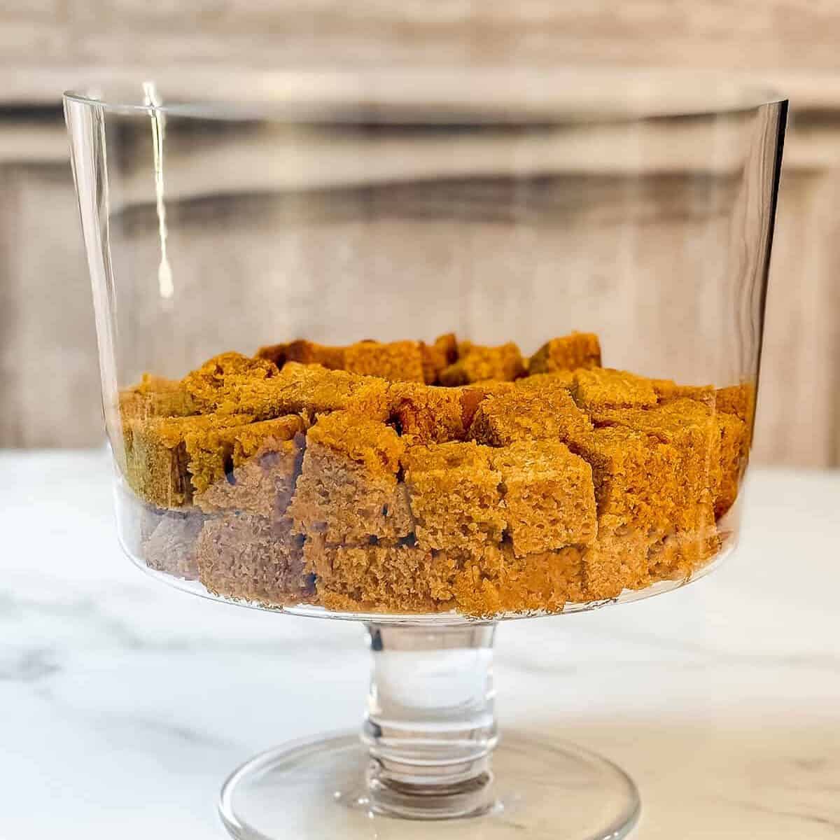 First layer of pumpkin bread in the base of a glass trifle dish.