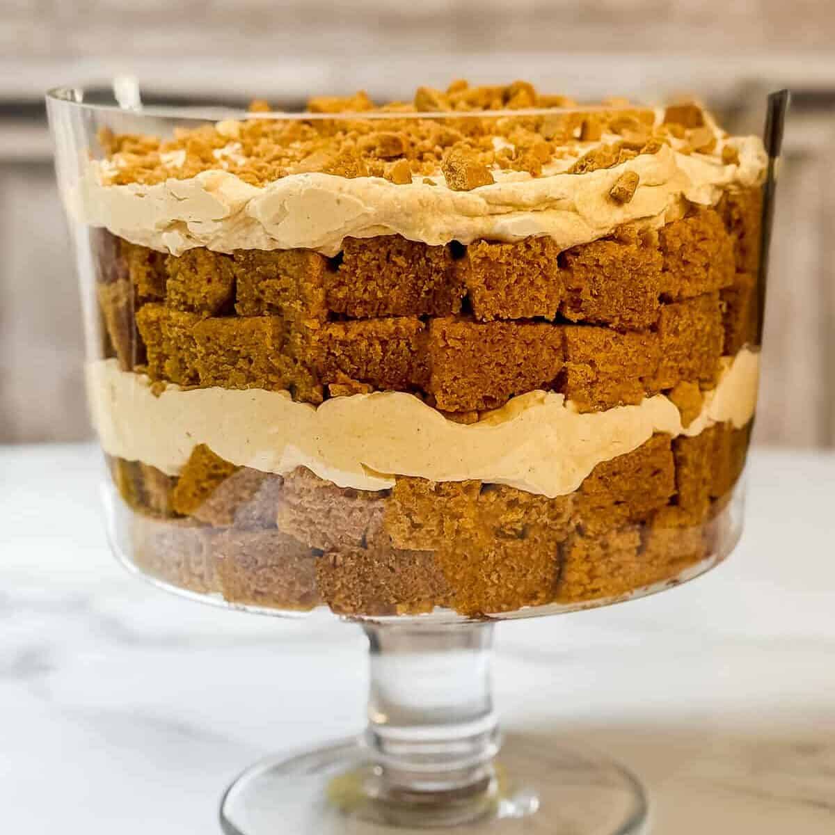 Fourth and final layer of pumpkin Chantilly cream and crumble cookies in a glass trifle dish.