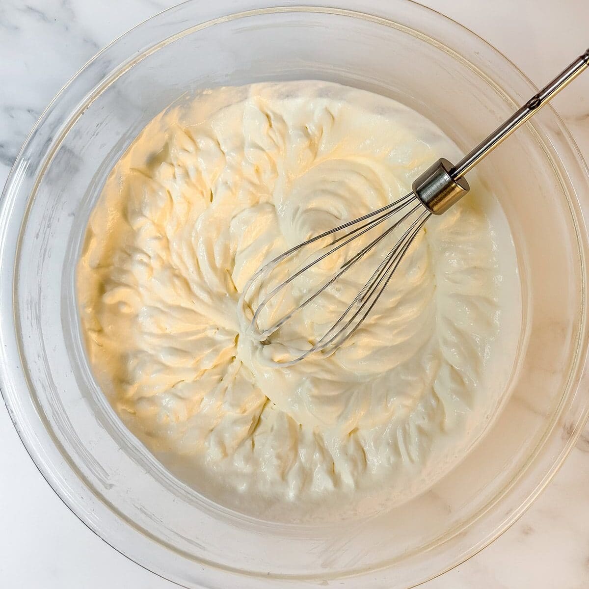 Whipped Chantilly Cream base layer in a glass bowl with a whisk.