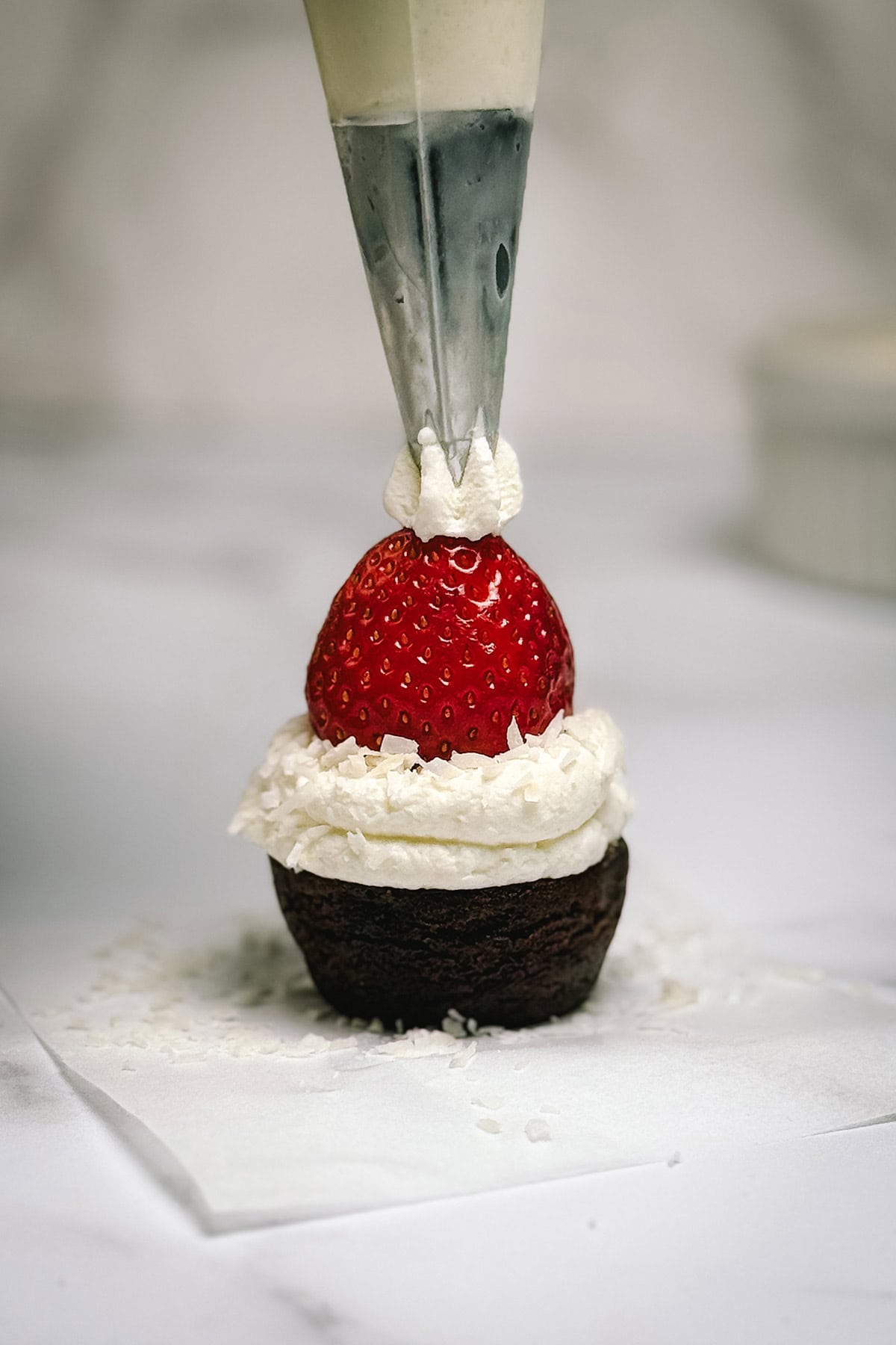 Piping a small dollop of whipped cream onto the strawberry tip to complete the Santa hat brownie bite.