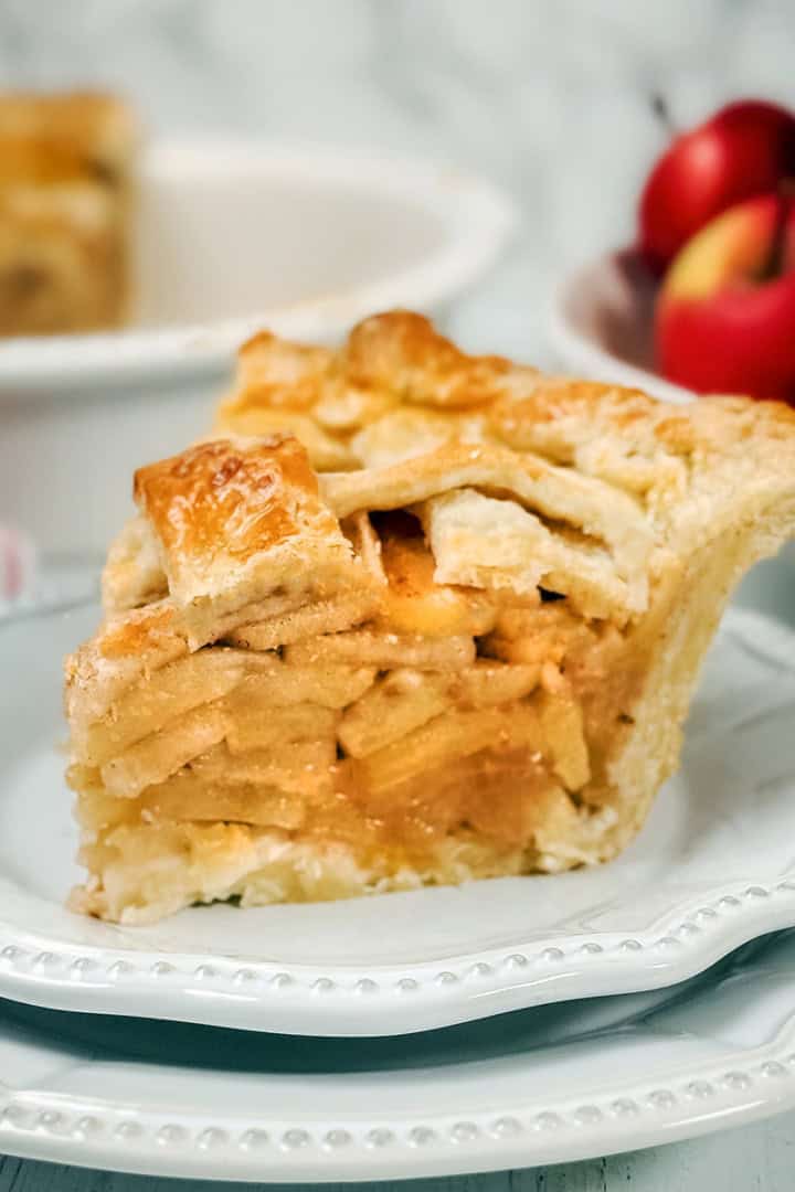 Square image of sliced apple pie with fresh apples in the background and a sliced apple pie.