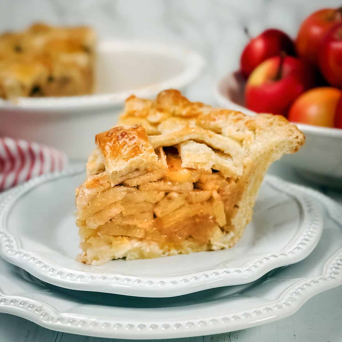 Square image of sliced apple pie with fresh apples in the background and a sliced apple pie.