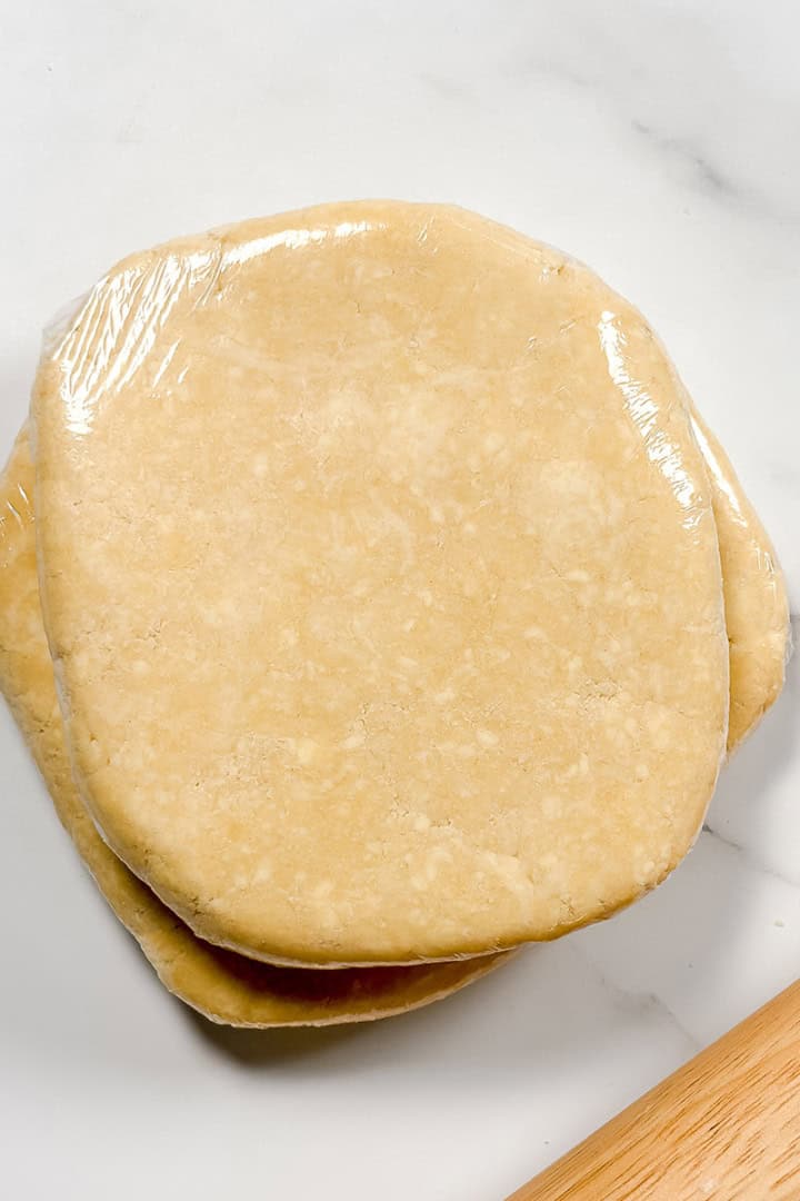 Square image of chilled and wrapped all butter crust with a rolling pin.