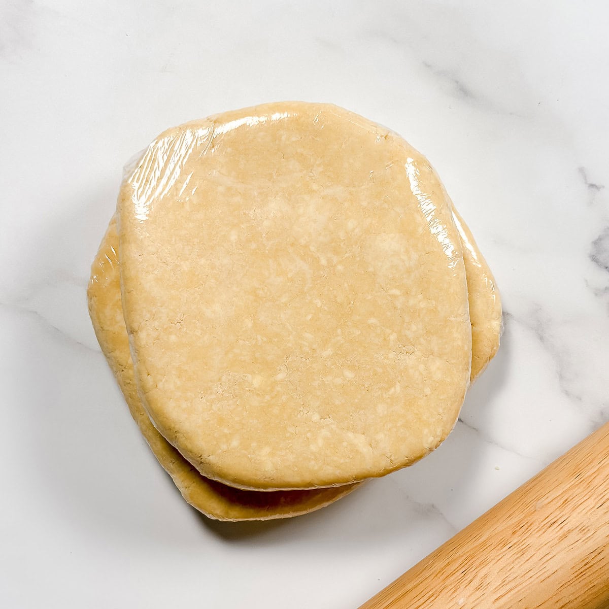 Square image of chilled and wrapped all butter crust with a rolling pin.