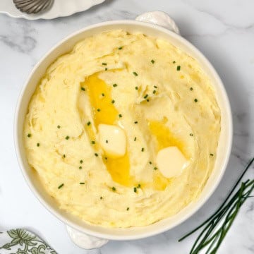 Square image of creamy garlic mashed potatoes in a white handled casserole dish with fresh snipped chives.