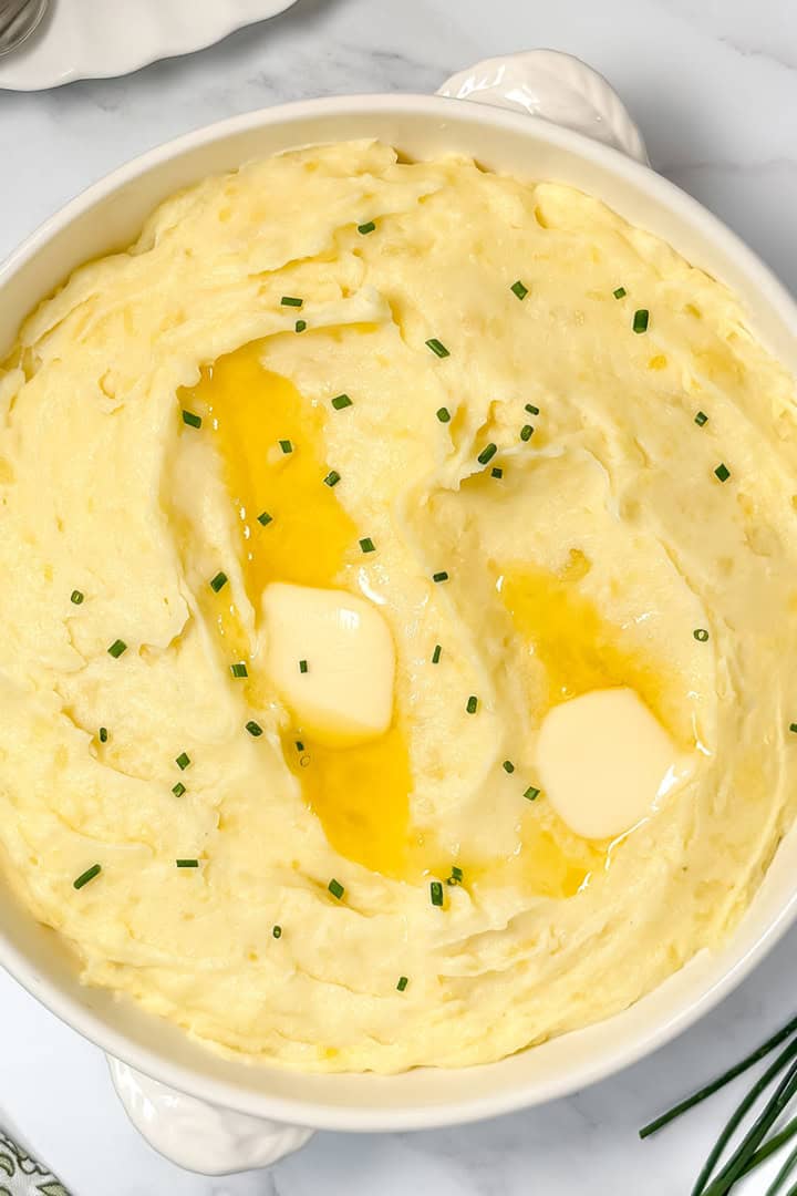 Square image of creamy garlic mashed potatoes in a white handled casserole dish with fresh snipped chives.
